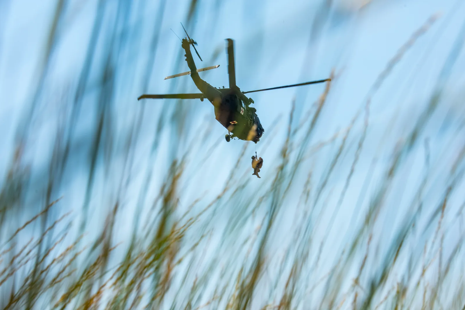 Idaho Army National Guard UH-60 Black Hawk hoists two people, seen through tall grass, photo by Rusty Rehl