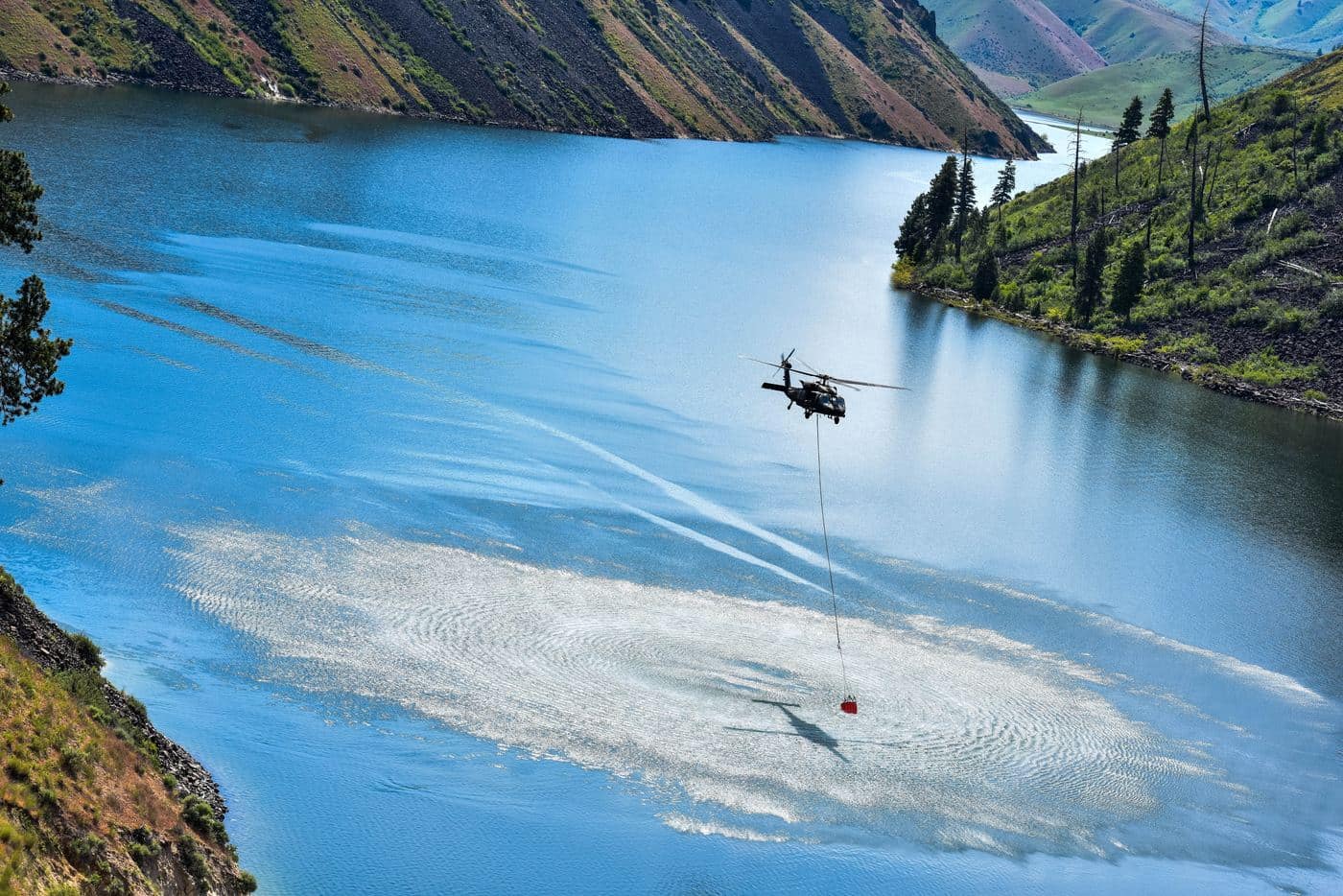 Idaho Army National Guard Black Hawk carries a water bucket over an Idaho reservoir, photo by Rusty Rehl