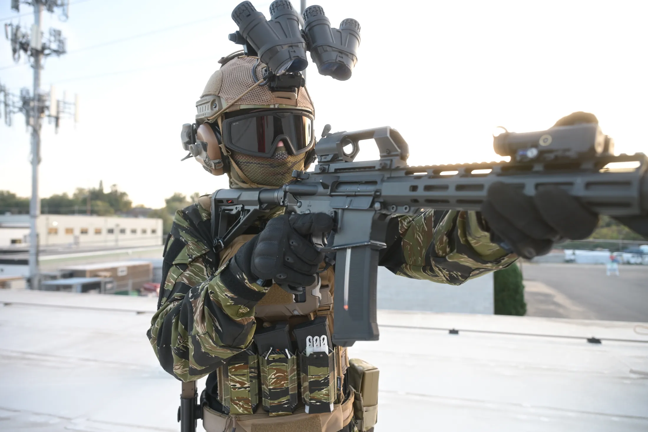 Commando in tiger-stripe camouflage aiming a rifle on a rooftop at golden hour, from Rusty Rehl's Combat Sport Supply ad