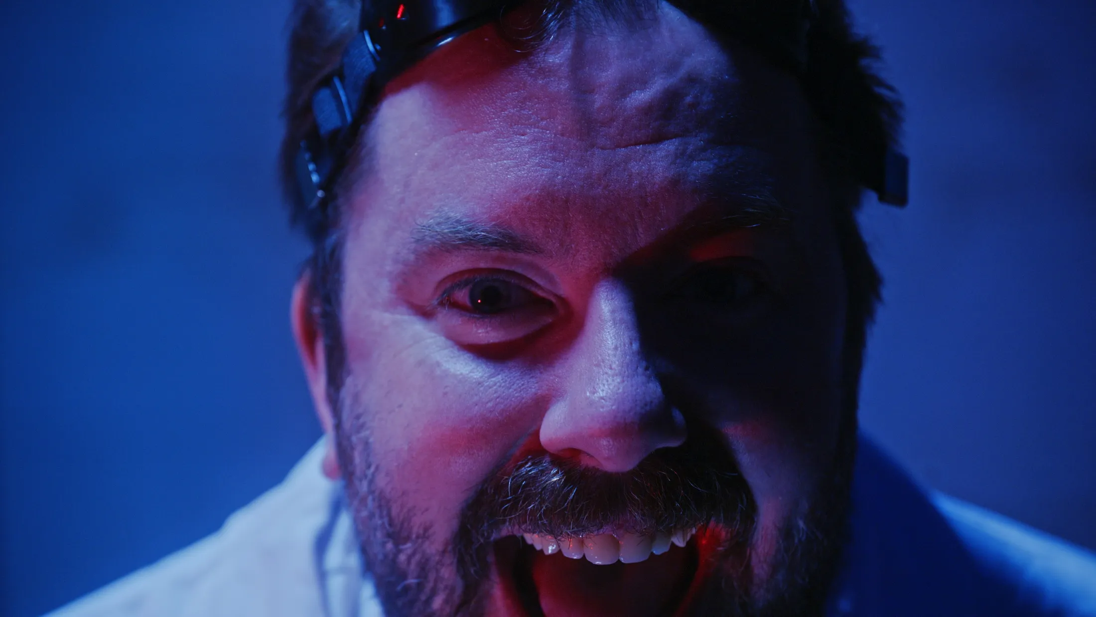 Close-up of the mad scientist's manic grin in blue and red light, still from Rusty Rehl's Combat Sport Supply ad