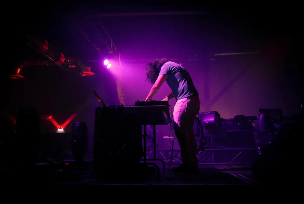 DJ bent over the decks in purple stage light, live concert photo by Rusty Rehl