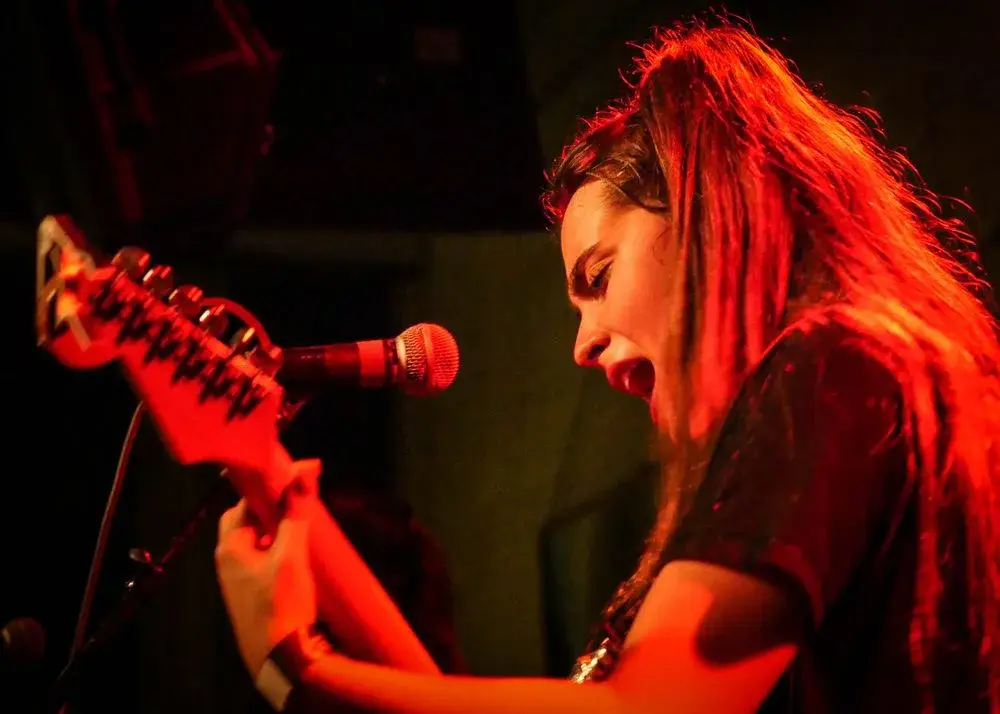 Hinds guitarist singing under red stage light, live concert photo by Boise, Idaho photographer Rusty Rehl