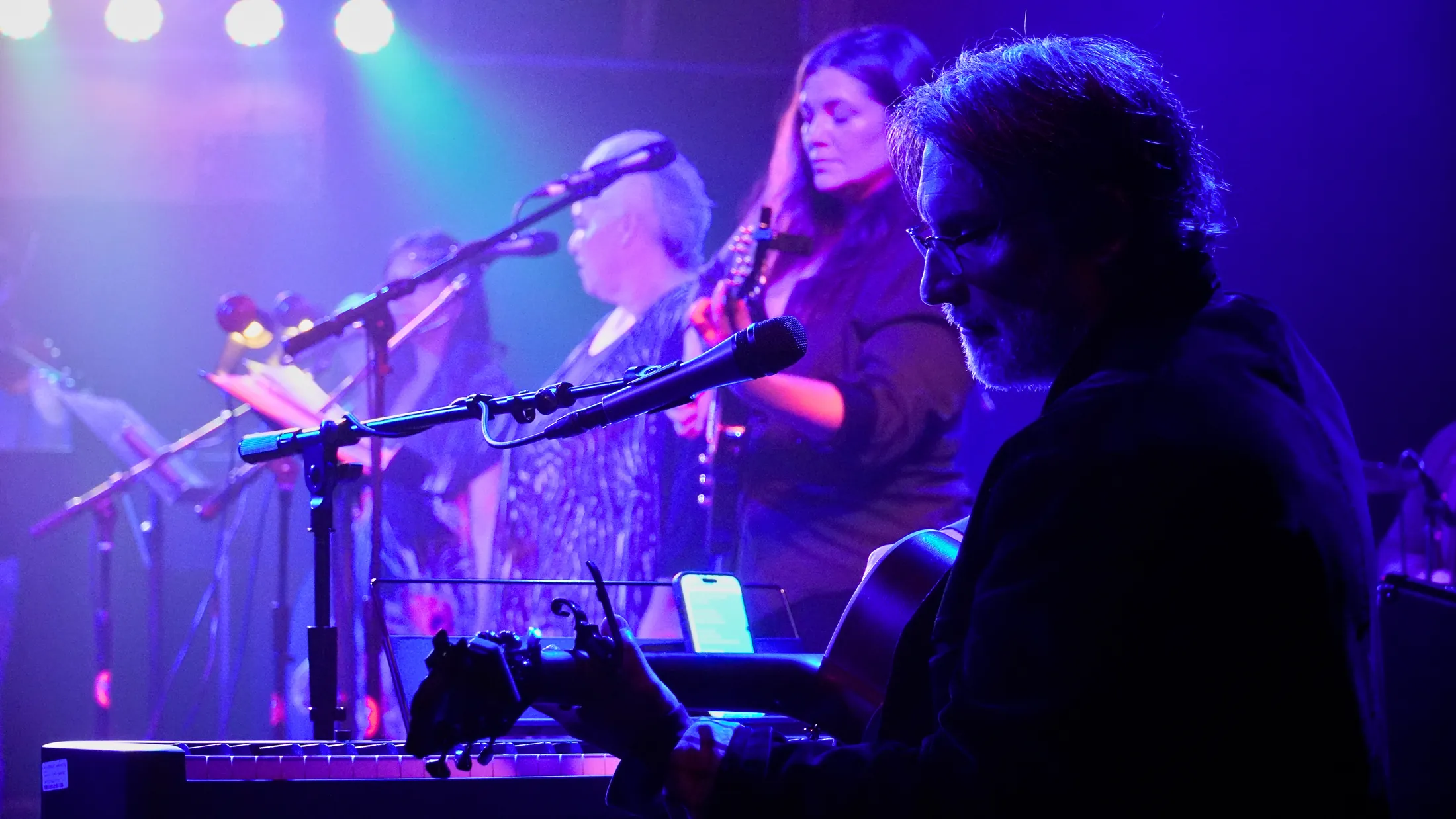 Martin Daniels with guitar while singers harmonize behind him, Boise, Idaho concert photo by Rusty Rehl