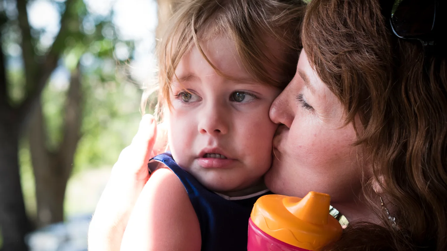 Mother kissing her toddler on the cheek in summer shade, candid family photo by Boise, Idaho photographer Rusty Rehl